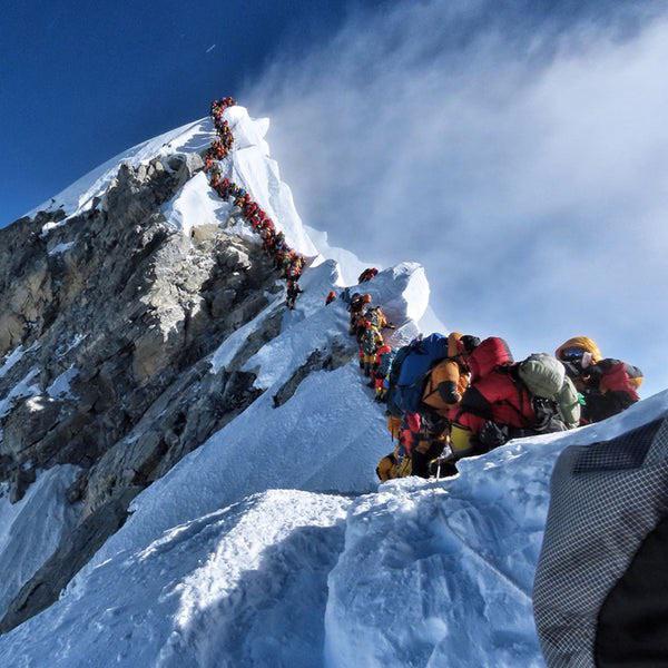 Climbers ascending snowy Mount Everest summit ridge with rocky peak and blue sky