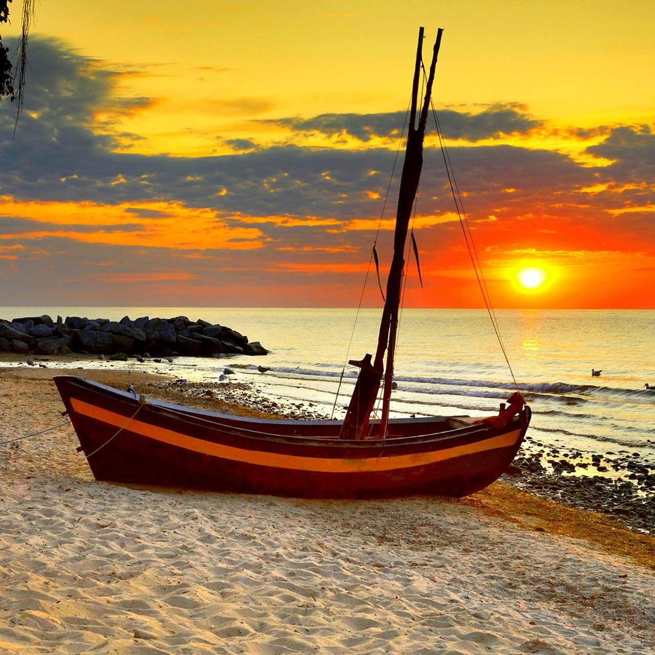 Wooden sailboat with red and yellow stripes on beach during golden sunset over ocean