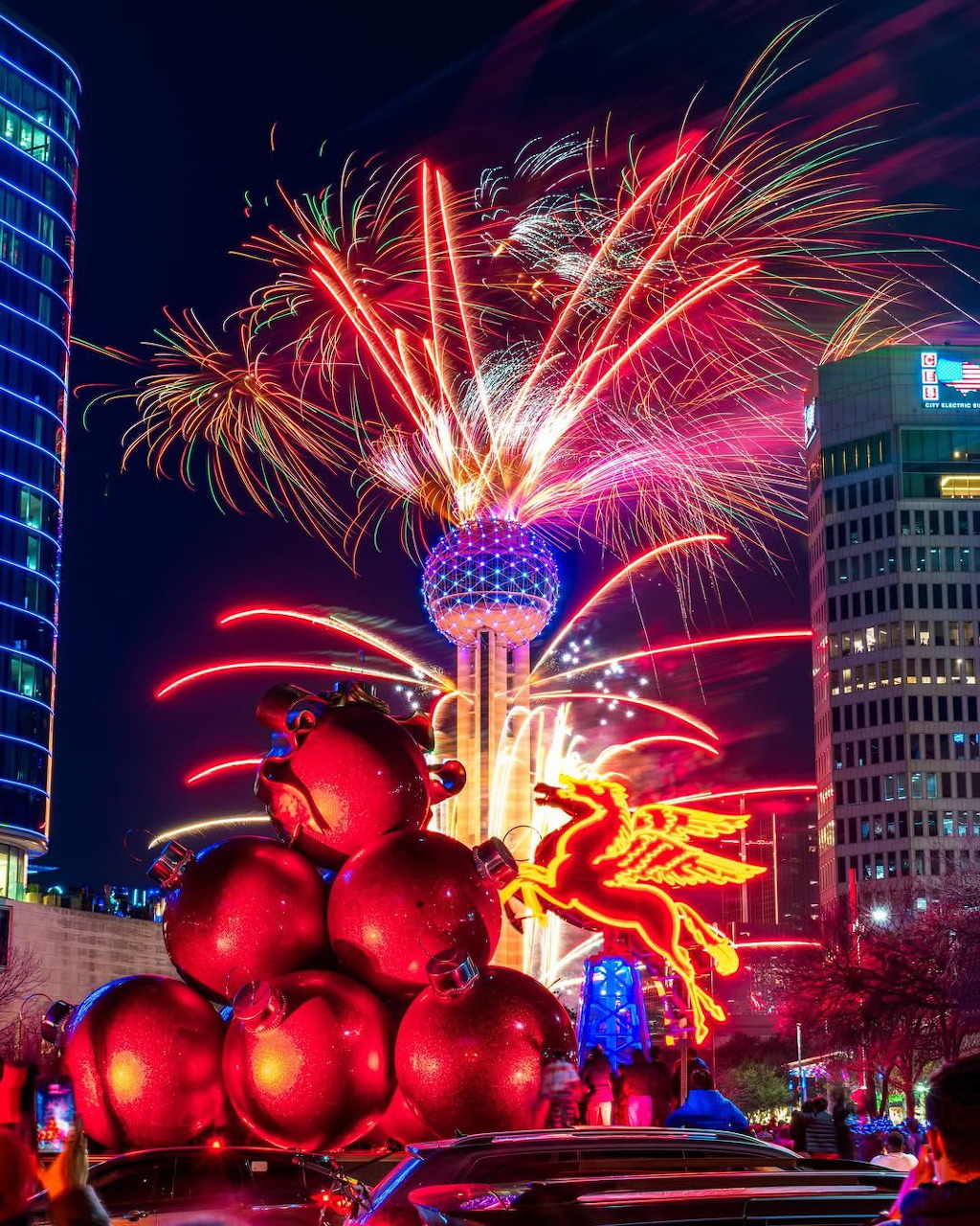 Fireworks over Dallas Reunion Tower with giant red ornaments and neon Pegasus sign at night