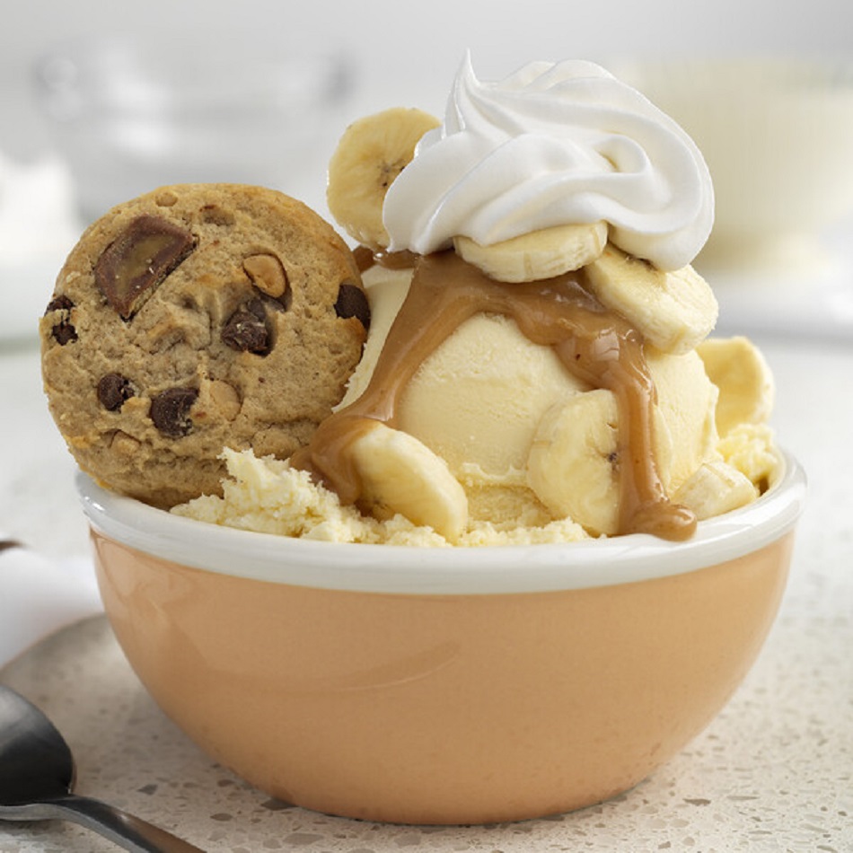 Bowl of vanilla ice cream with caramel drizzle, whipped cream, banana slices, and chocolate chip cookie