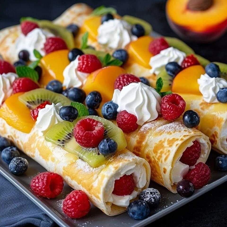 Platter of rolled crepes topped with whipped cream and assorted fresh berries and fruit slices