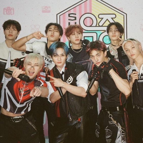 Seven young men posing together in colorful stage outfits indoors