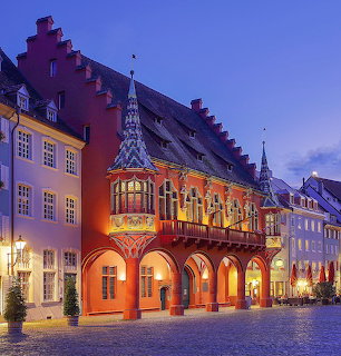 Illuminated red brick merchant's hall with gothic arcades and ornate tower at dusk in historic German city square