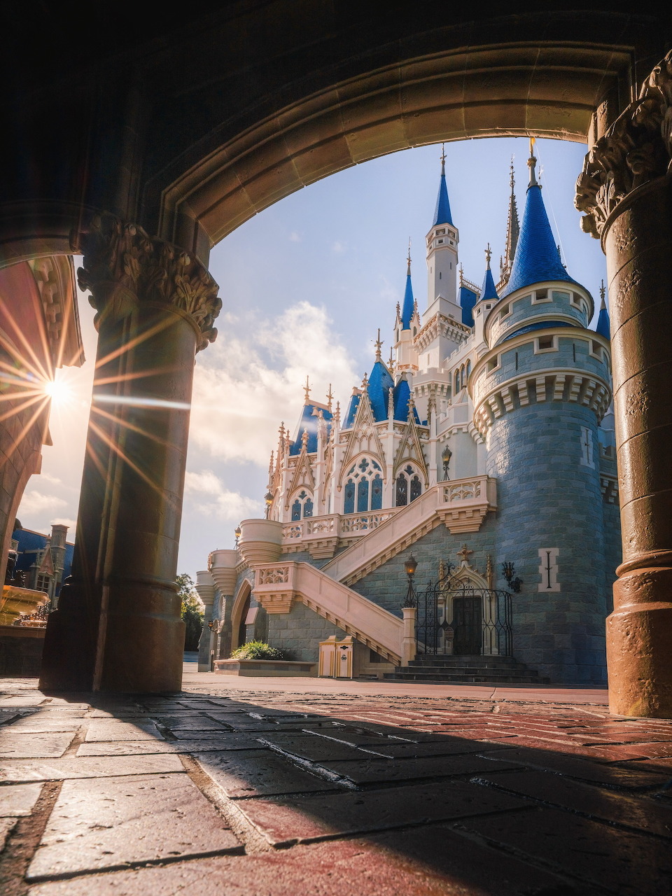 Fairy tale castle with blue turrets and ornate details viewed through stone archway with dramatic sunburst