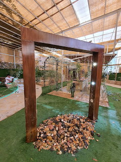 Wooden frame structure over rock pile in a greenhouse interior with green floor and glass panels