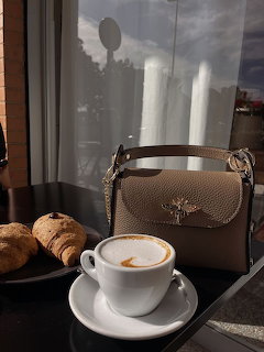 Cup of cappuccino on a table with croissants and a beige handbag by a window