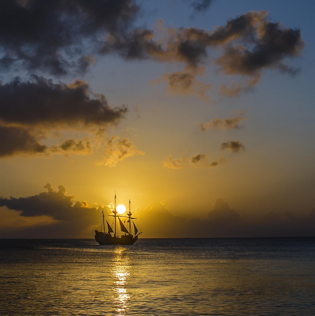 Silhouette of a sailing ship on the ocean at sunset with dramatic cloudy sky