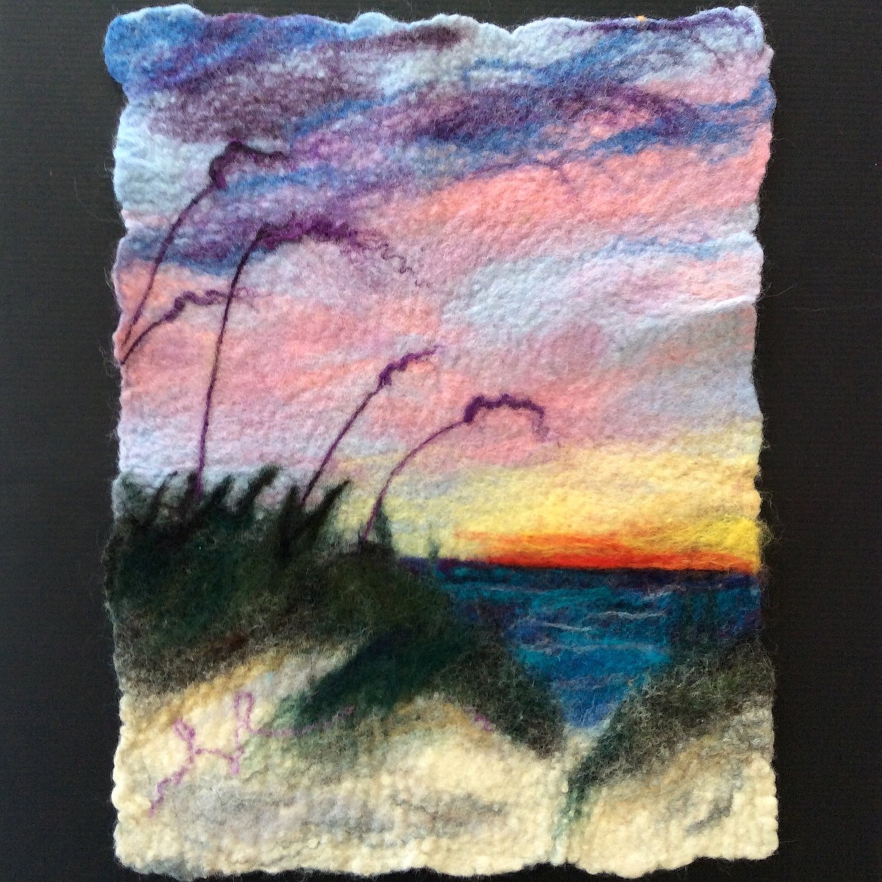 Textured fiber art showing sunset over water with silhouetted grass and trees in pink, purple, and orange tones