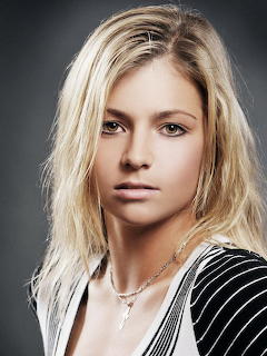 Portrait of blonde woman with wavy hair in striped top against gray background