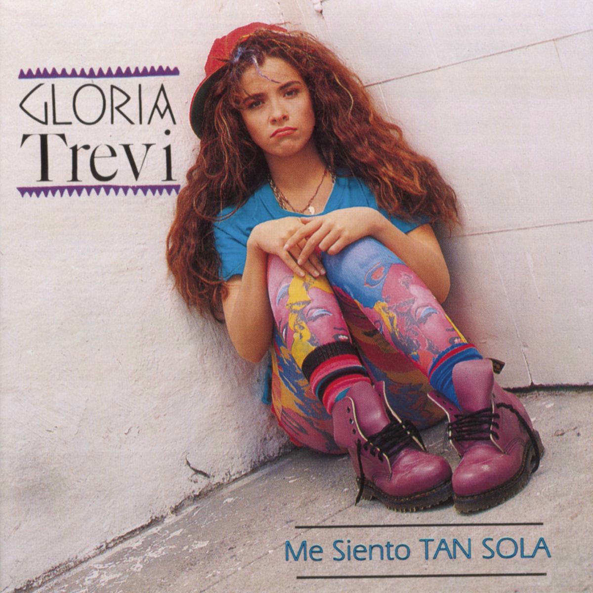Young woman with long curly hair sitting against a wall in colorful tights and boots, with Gloria Trevi text