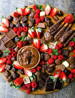 Chocolate dessert board with strawberries, chocolates, wafer rolls, and dipping sauce on rustic wood background