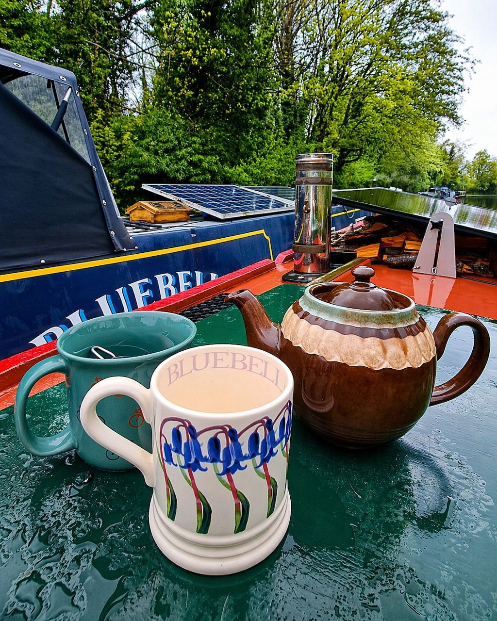 Ceramic teapot and Bluebell mug on a narrowboat deck with a canal and green trees in the background