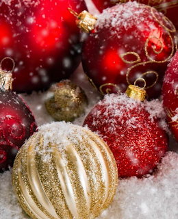 Red and gold glittery Christmas ornaments nestled in white snow with sparkling bokeh lights
