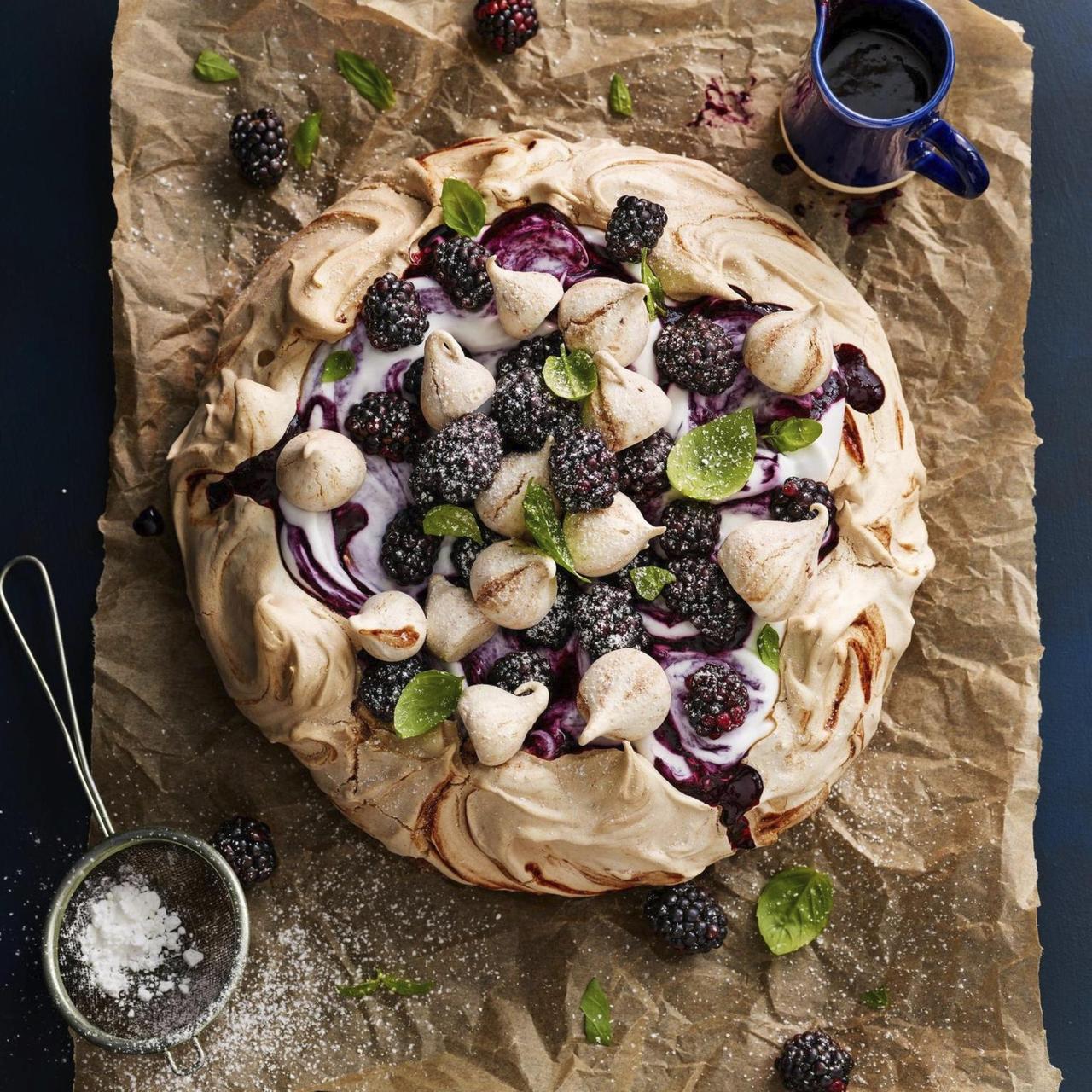 Meringue pavlova dessert topped with blackberries, figs, almonds, and mint on rustic parchment paper