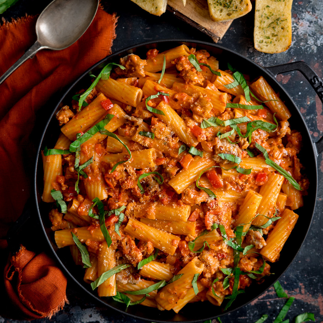 Overhead view of rigatoni pasta in tomato meat sauce with basil in a black skillet