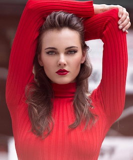 Portrait of a woman in a bright red long-sleeve top with her arms raised above her head.