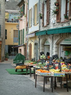 Narrow street in Vence France with outdoor fruit and vegetable market stalls beside old buildings