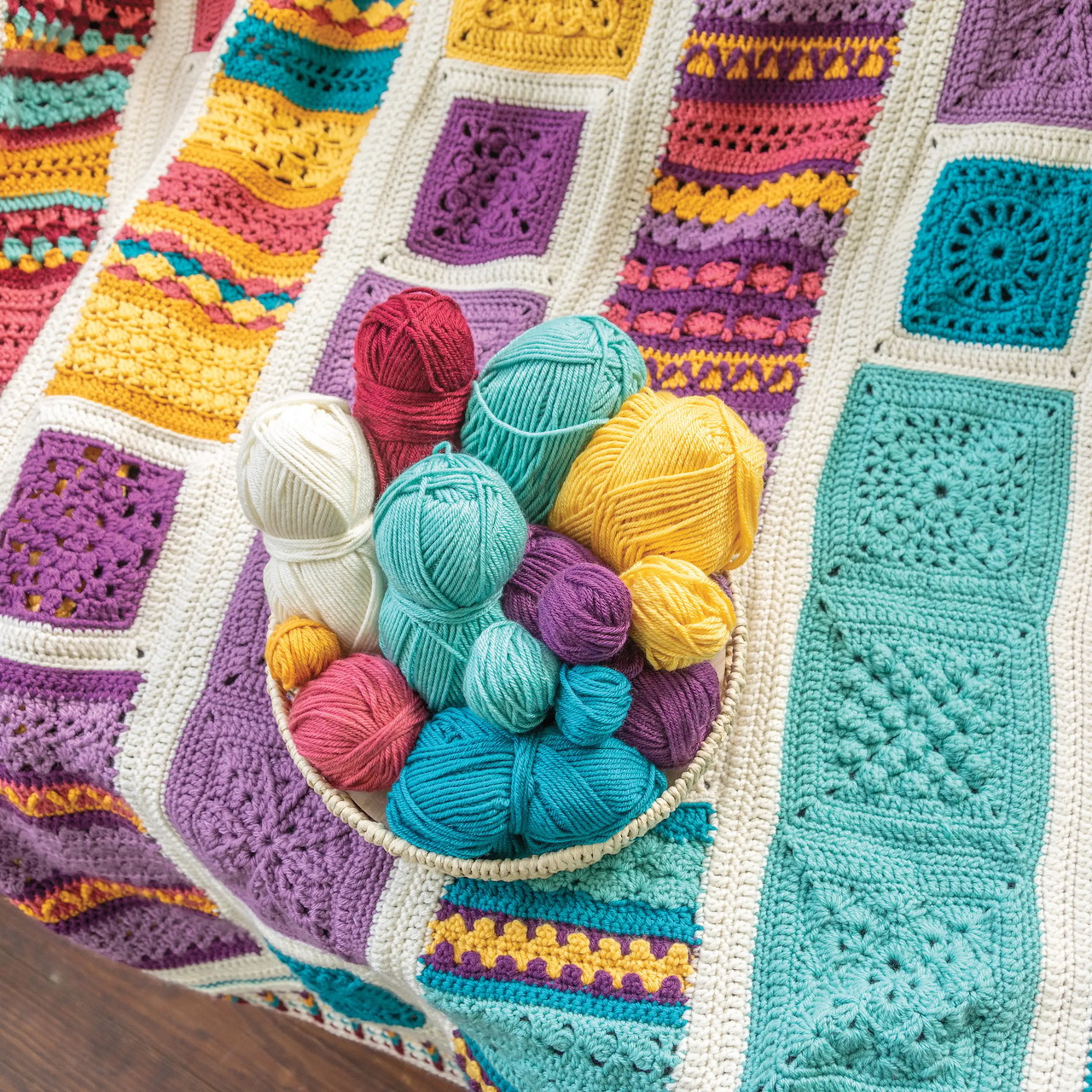 Colorful crochet afghan blanket with granny squares and striped patterns, yarn balls arranged on top