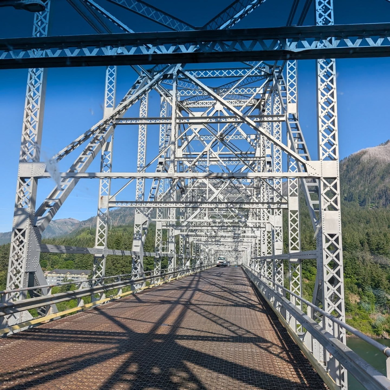 Steel truss bridge viewed from the center with mountains and blue sky in the background