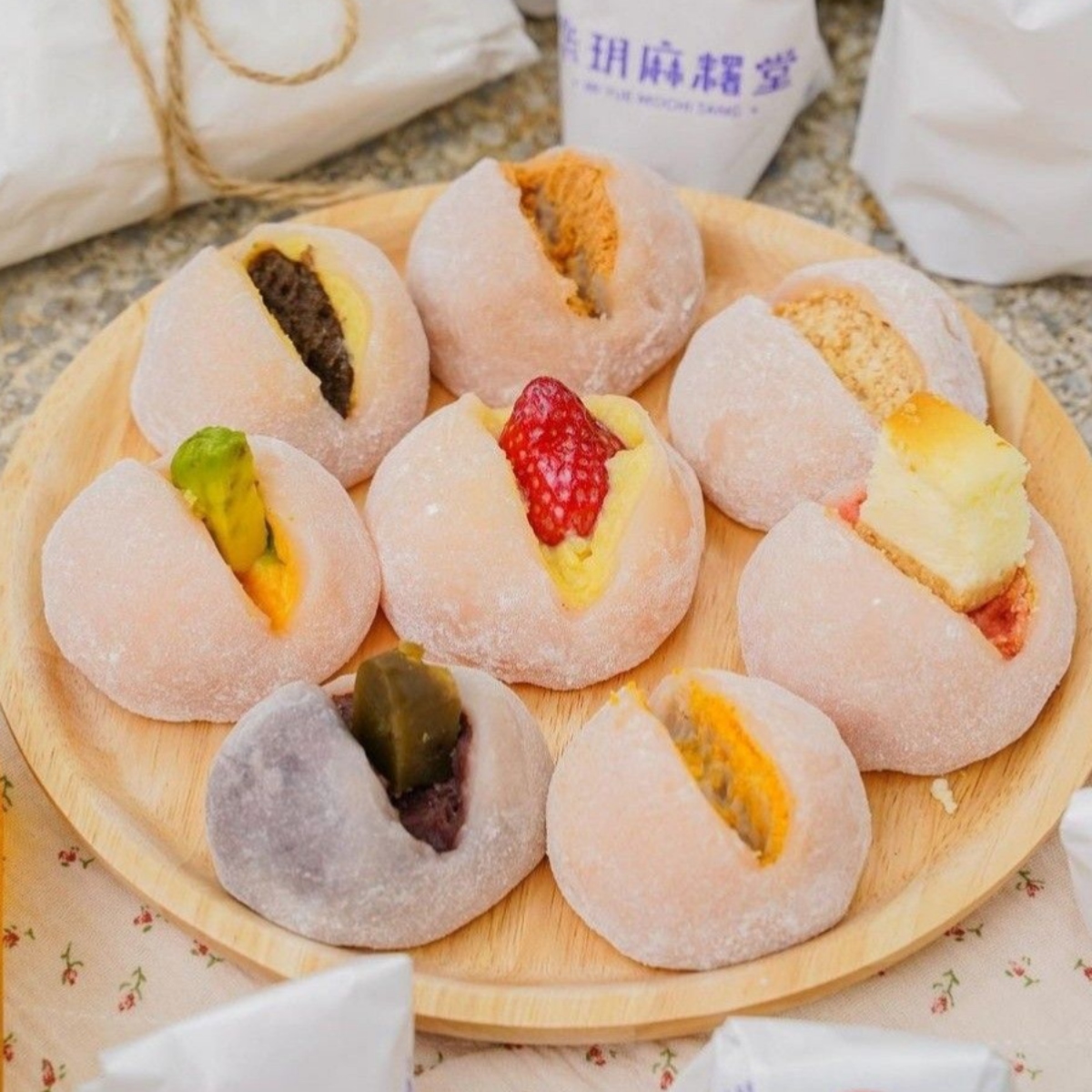 Assorted pastel mochi with fruit and cream fillings on a round wooden plate