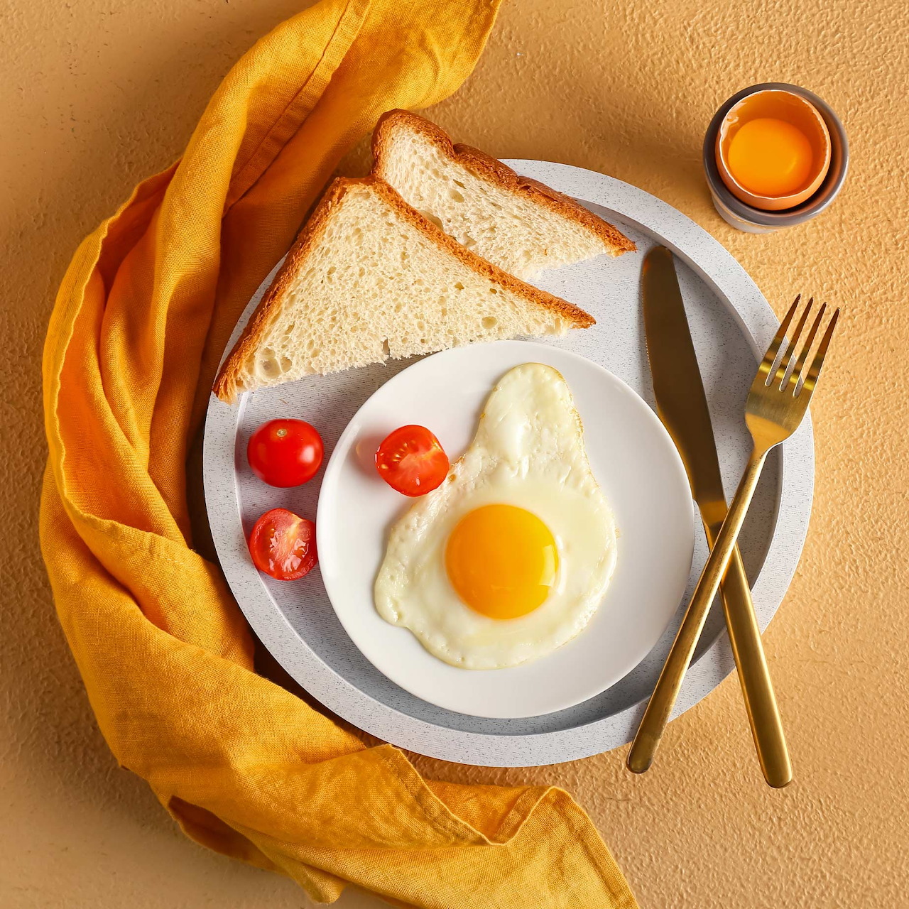 Overhead view of breakfast plate with fried egg, toast, tomatoes, and orange juice on yellow background