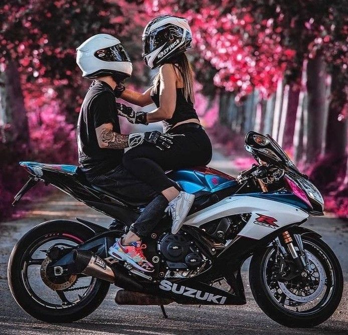 Couple in helmets sitting on a white Suzuki sport motorcycle with pink trees in the background