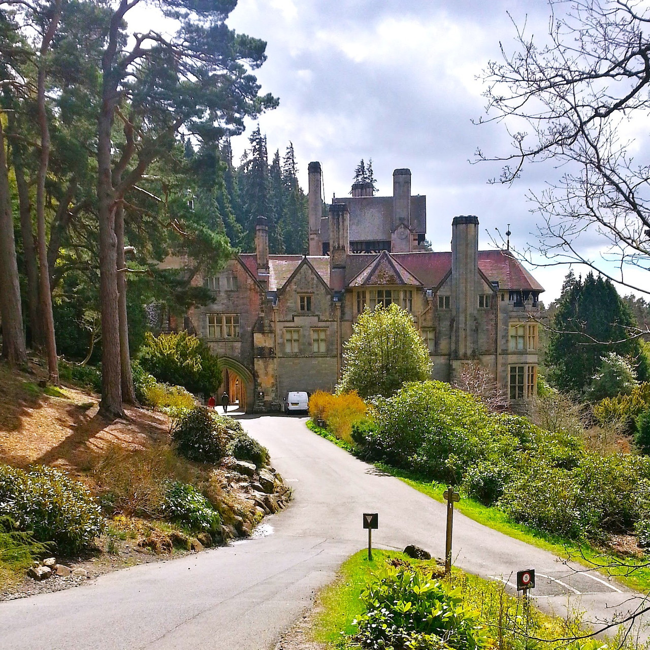 Cragside House, a Victorian stone mansion in Northumberland surrounded by gardens and trees under a cloudy sky