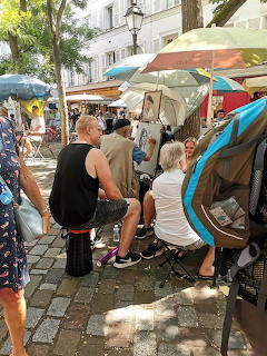 Street artist painting a portrait of a woman sitting under umbrellas on a cobblestone square