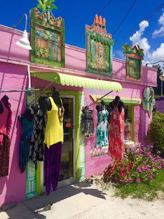 Pink beach clothing shop with colorful dresses hanging outside and decorative green signs