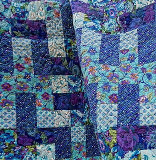 Patchwork quilt with blue, purple and floral fabric squares in traditional pattern