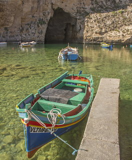 Colorful traditional Maltese fishing boats in a clear green cove surrounded by limestone cliffs