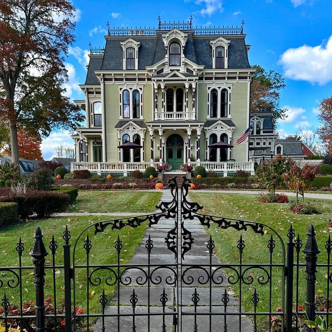 Victorian mansion with ornate facade, iron fence, and formal garden under blue sky