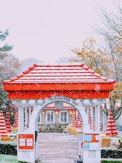 Decorative gazebo with red and white striped roof and columns during snowfall in a park