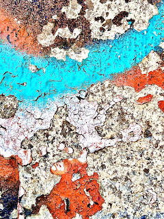Close-up of cracked and peling turquoise, orange, and white paint on a rough concrete surface