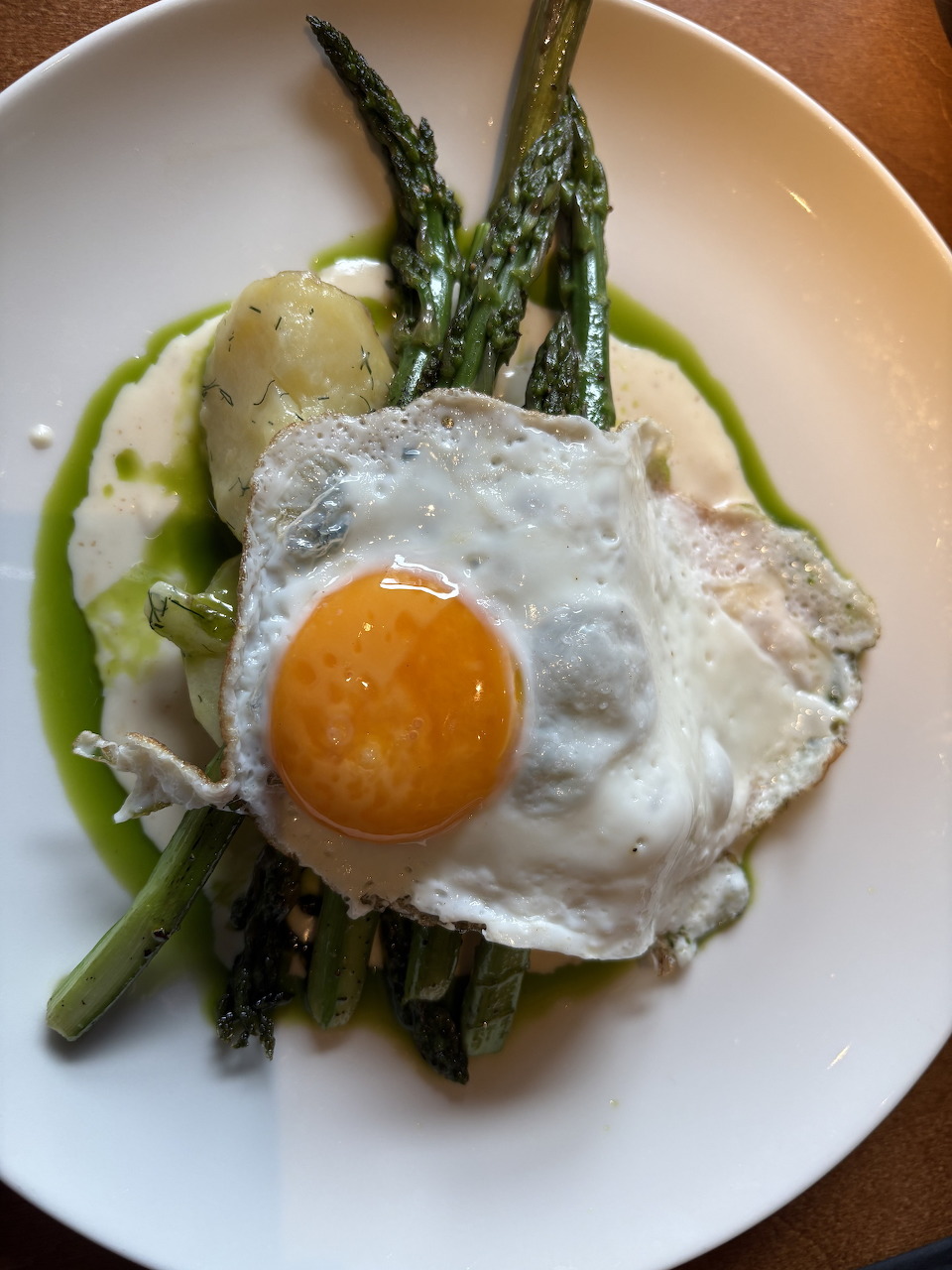 White plate with roasted asparagus,fried egg, mashed potatoes and green herb oil on a wooden table