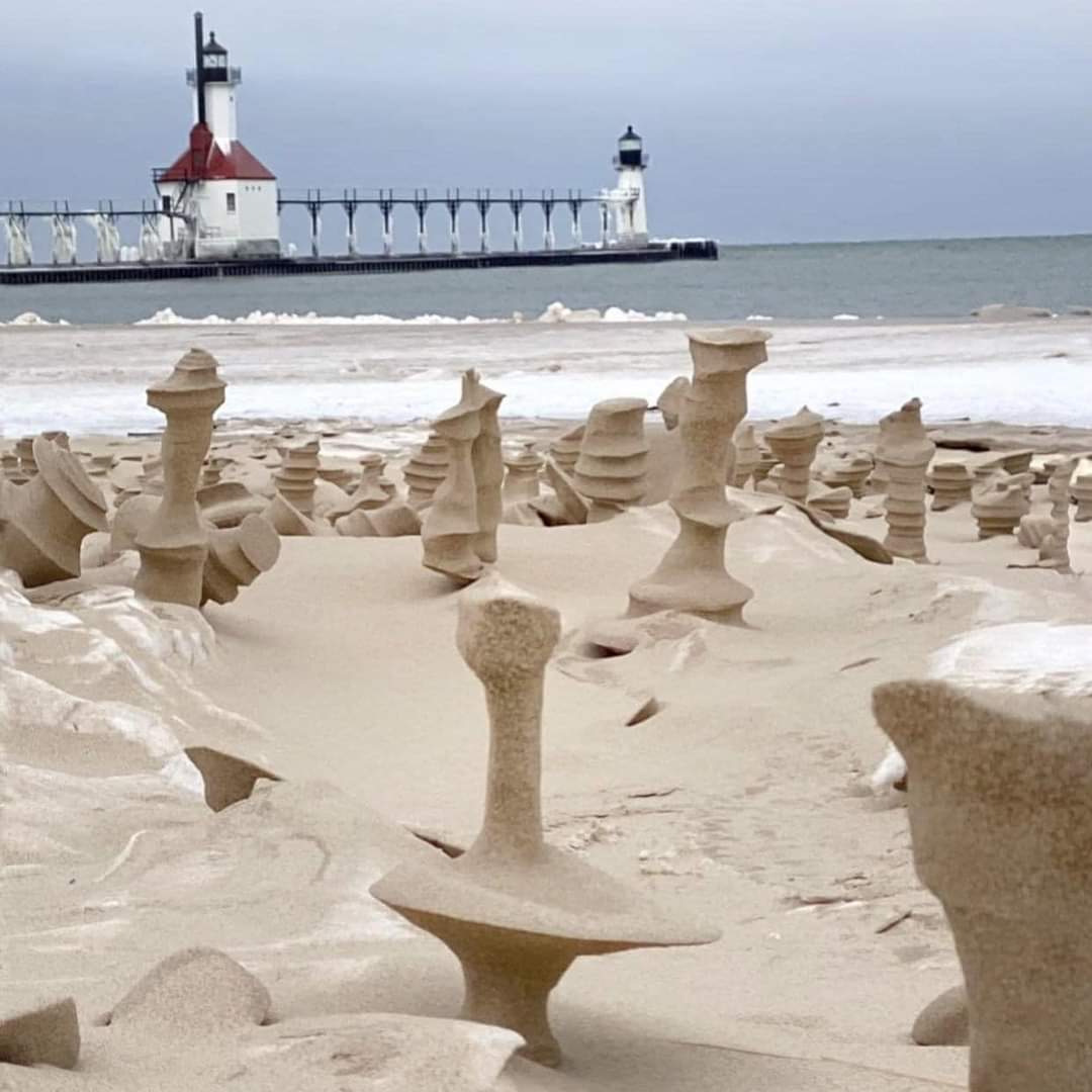 Sand sculptures on a beach with ocean waves and a lighthouse on a pier