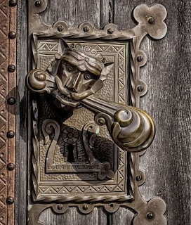 Close-up of an ornate antique brass door knocker with a bearded face on a rustic wooden door