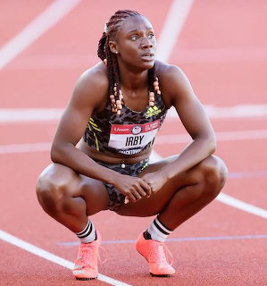 Female sprinter crouching on red track wearing racing kit and orange spikes