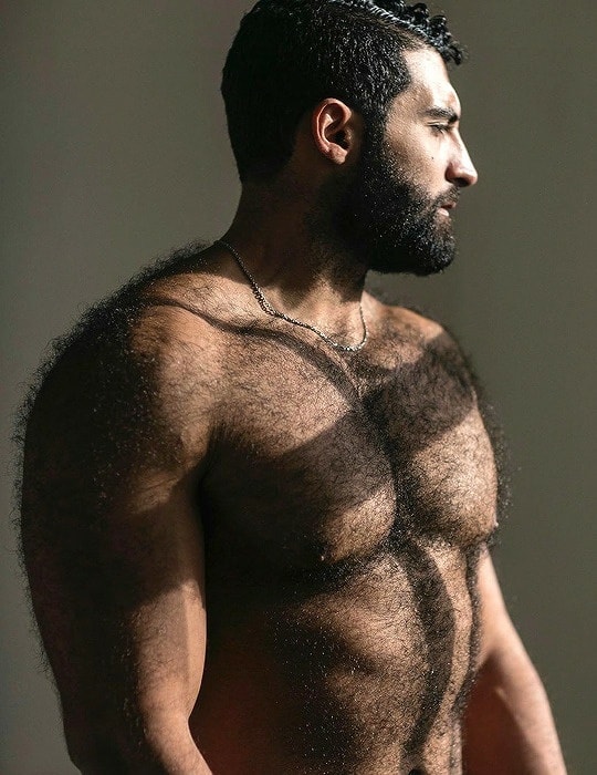 Side profile of a muscular bearded man with dark hair in a studio portrait