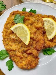 Two breaded schnitzel cutlets with lemon slices and parsley on a white plate