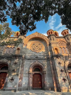 Ornate stone church facade in Mexico with rose window, arched doors, and trees framing the building