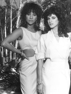 Two women in 1980s outfits posing together in front of tropical foliage in black and white