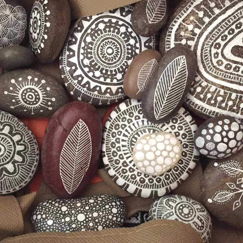 Collection of smooth stones painted with white mandala and geometric patterns on brown and gray surfaces