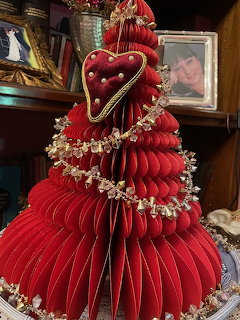 Red honeycomb paper Christmas tree with gold garland and heart ornament on a decorated table