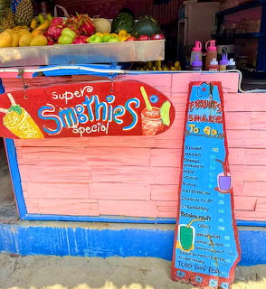 Colorful pink smoothie stand with hand-painted menu signs and fresh fruits displayed on top