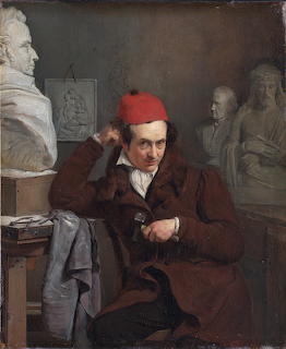 Oil painting of a man in a brown coat and red cap seated among marble busts in a sculptor's studio