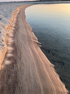 Aerial view of sandy beach barrier stretching into blue ocean water at sunset