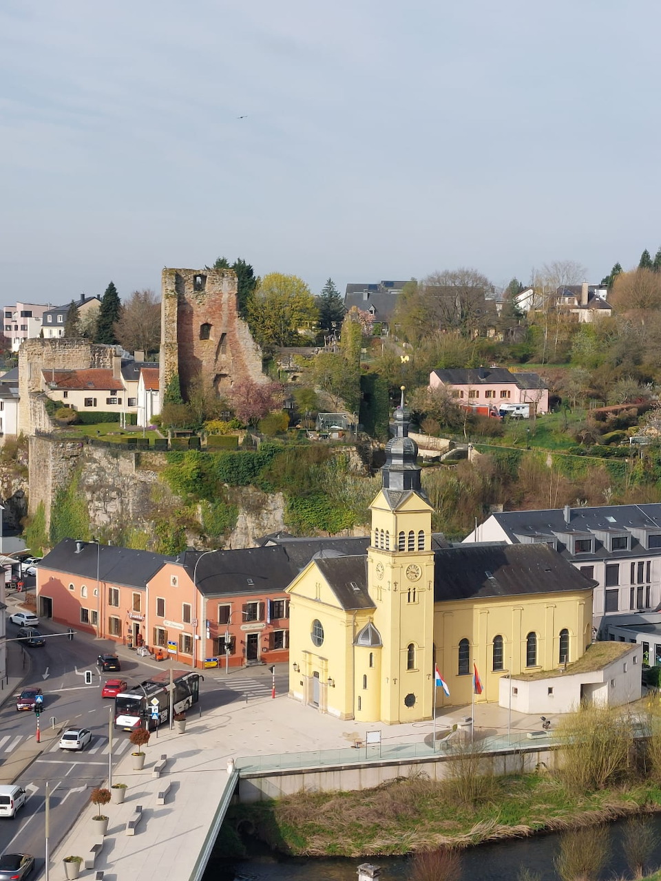 View of a small town with a yellow church, houses, and old tower ruins on a hillside
