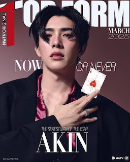 Portrait of a young man with dark hair holding a playing card against a brown background