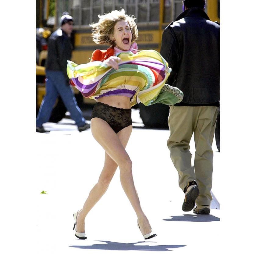 Woman in colorful flowing skirt dancing on street with pedestrians in background